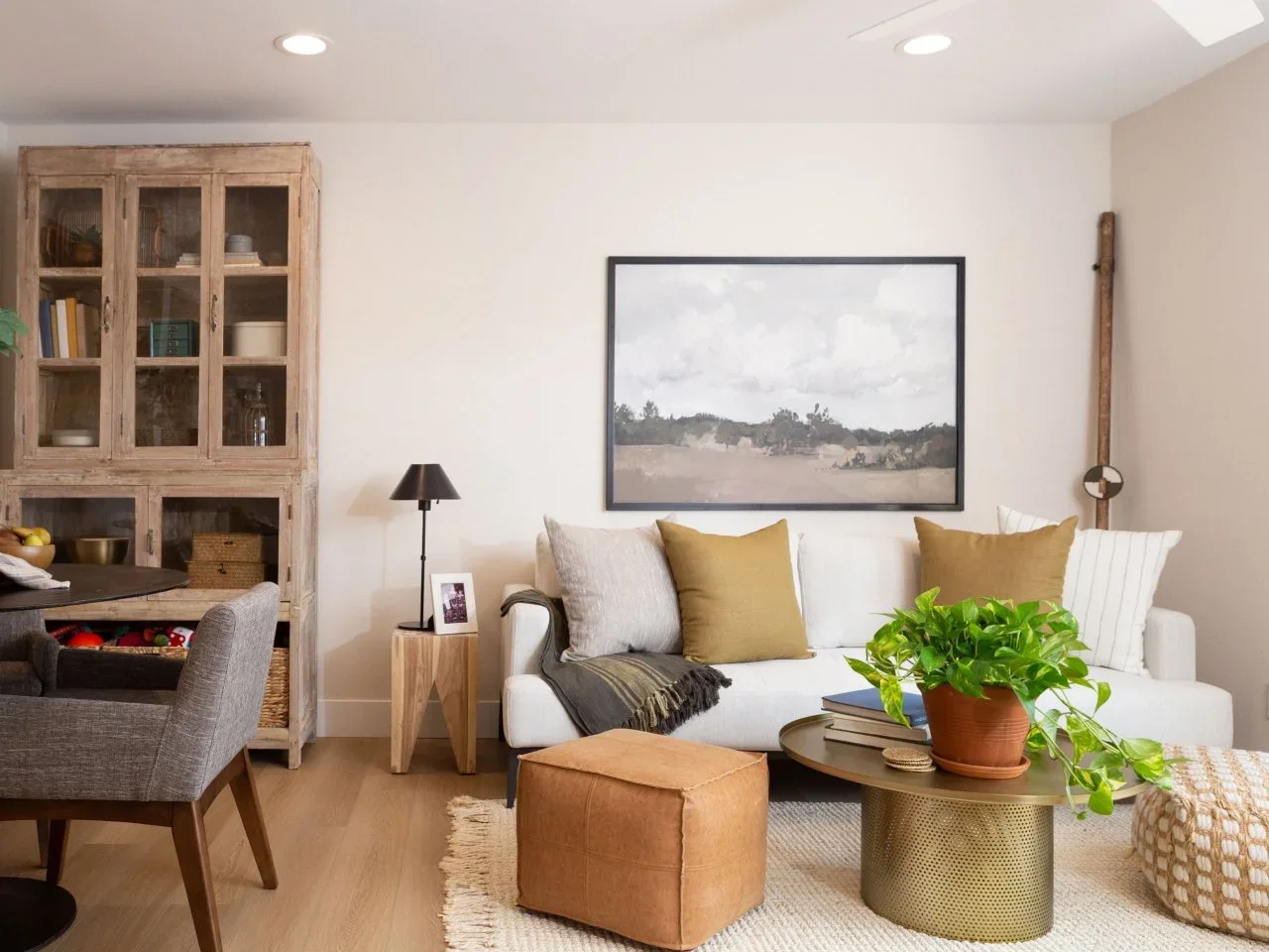 A cream sofa with muted green cushions sits beside a tall timber display cabinet and tan cube ottoman.