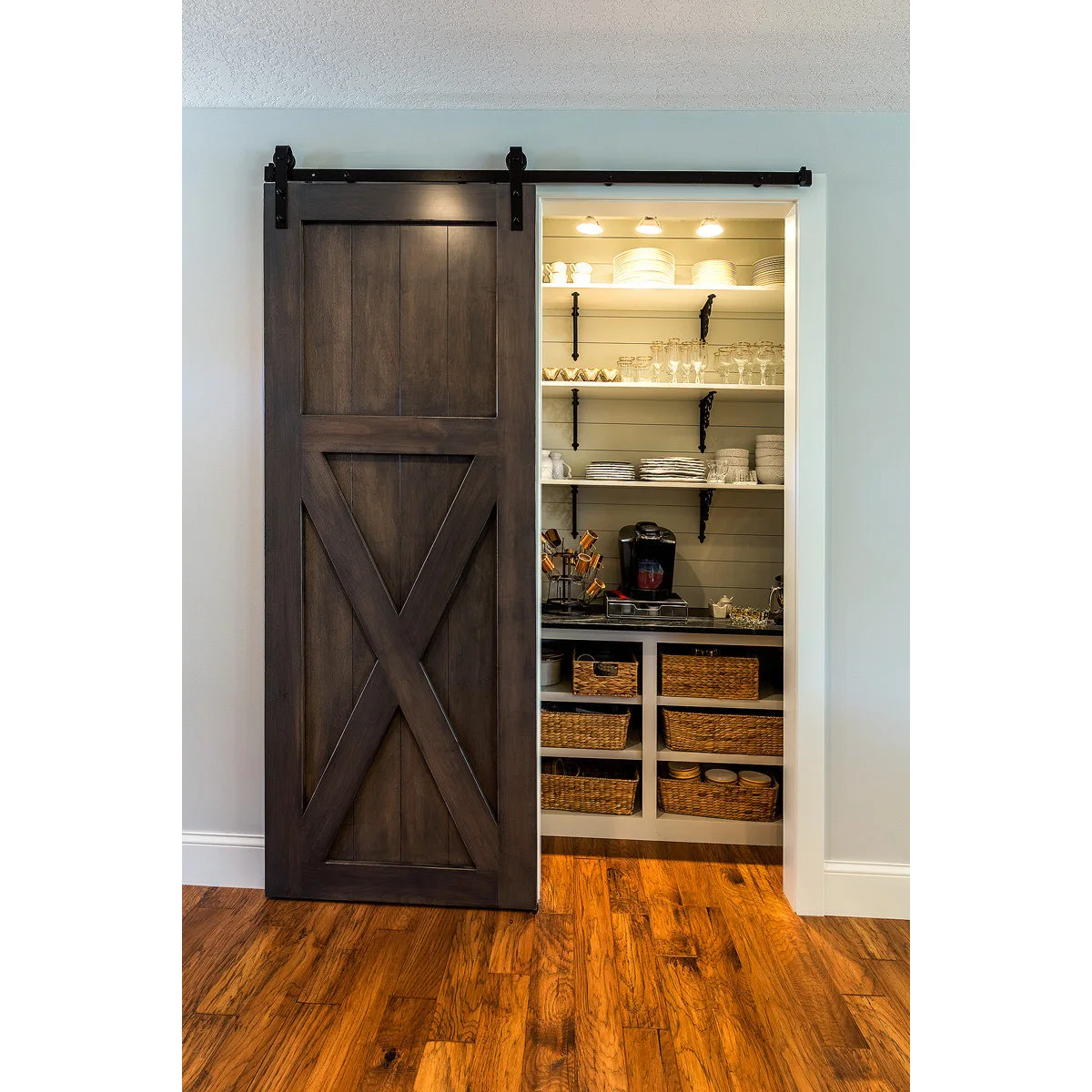 A dark wood sliding door reveals white shelves, glasses, a drinks counter and baskets in a shallow recessed pantry.