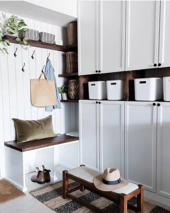 White paneled cabinet fronts with a row of white bins, dark wood shelves and a small hook-and-seat area to the side.