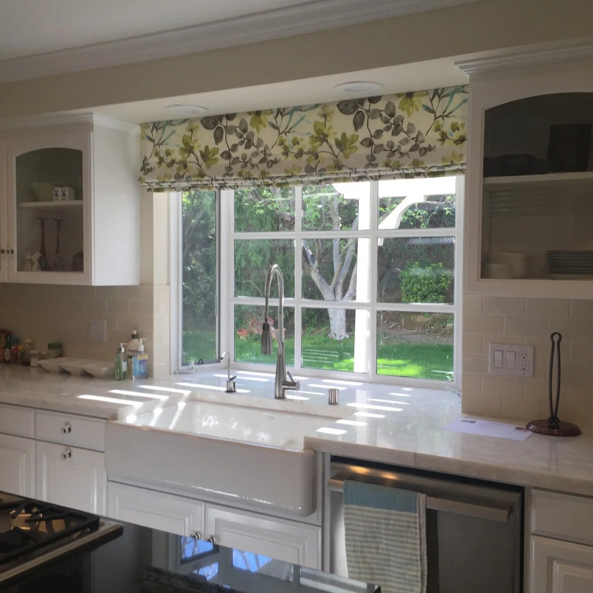 Leaf-pattern fabric shade above a farmhouse sink between white kitchen cabinets