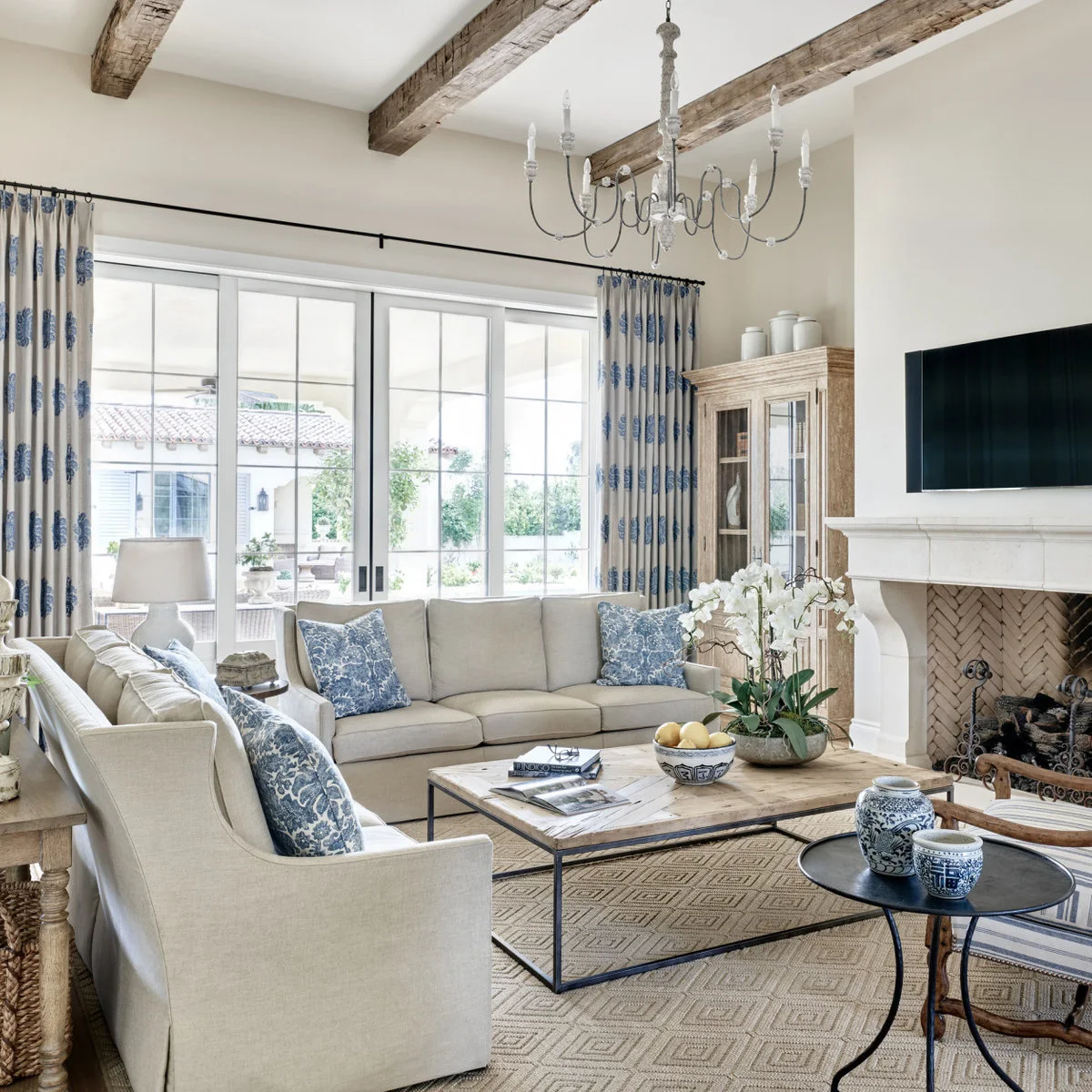 Two pale sofas form an L around a rectangular wood-topped table, with a striped chair on the open side near the fireplace.