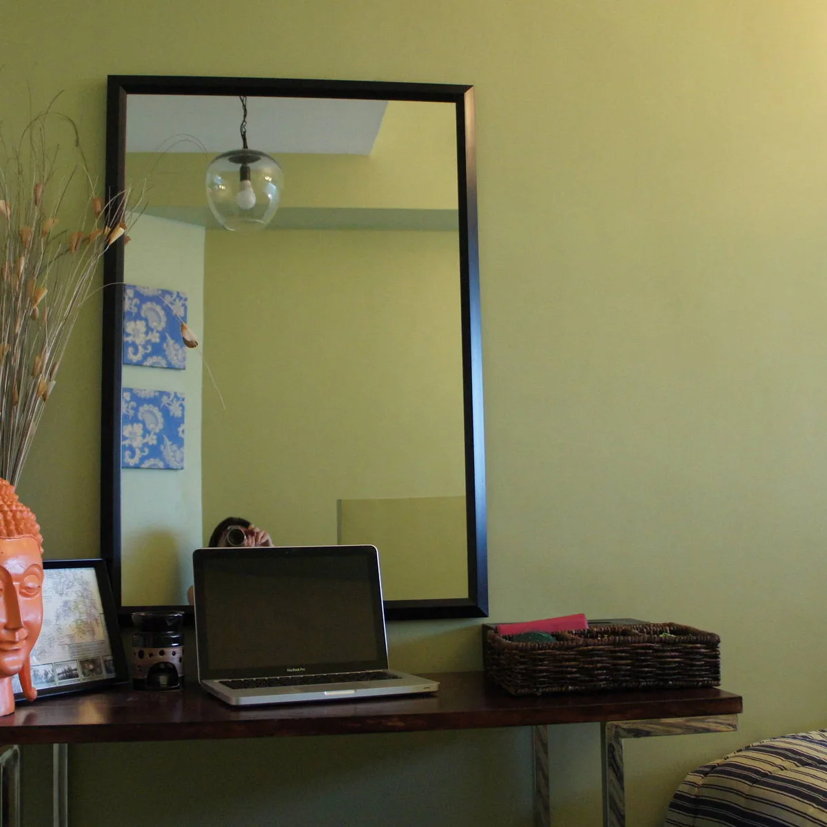 Narrow wall-mounted wood desk with a laptop, woven tray and large black-framed mirror