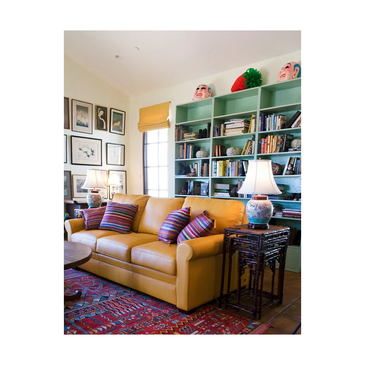 Mustard sofa with striped cushions in front of pale green bookcases and a patterned red rug