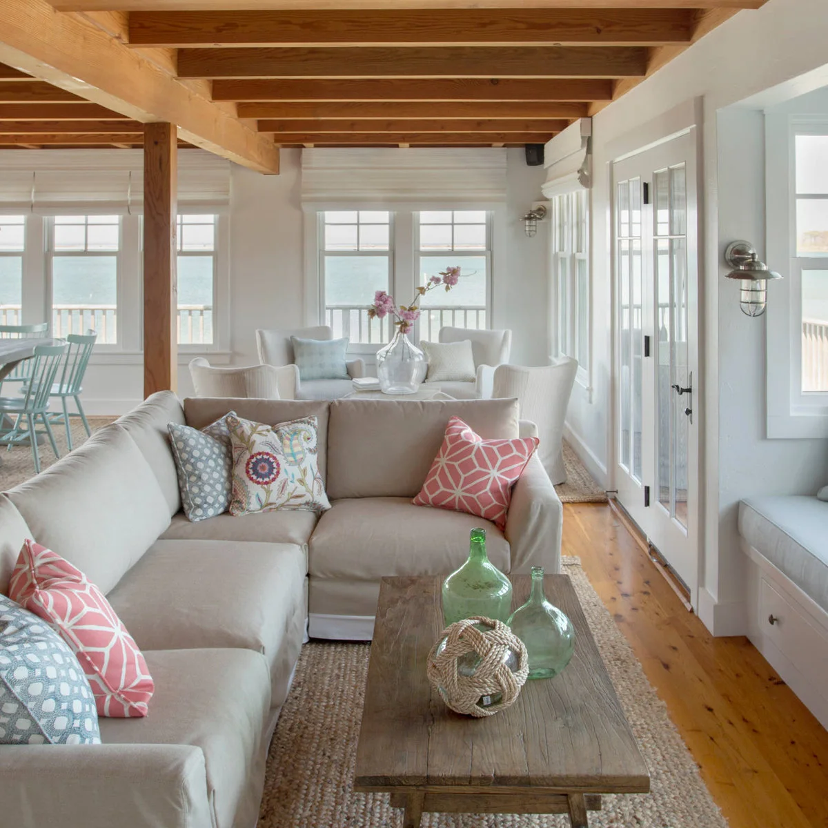 Warm gray sectional with blush pink and pale blue patterned cushions beneath exposed wood ceiling beams.