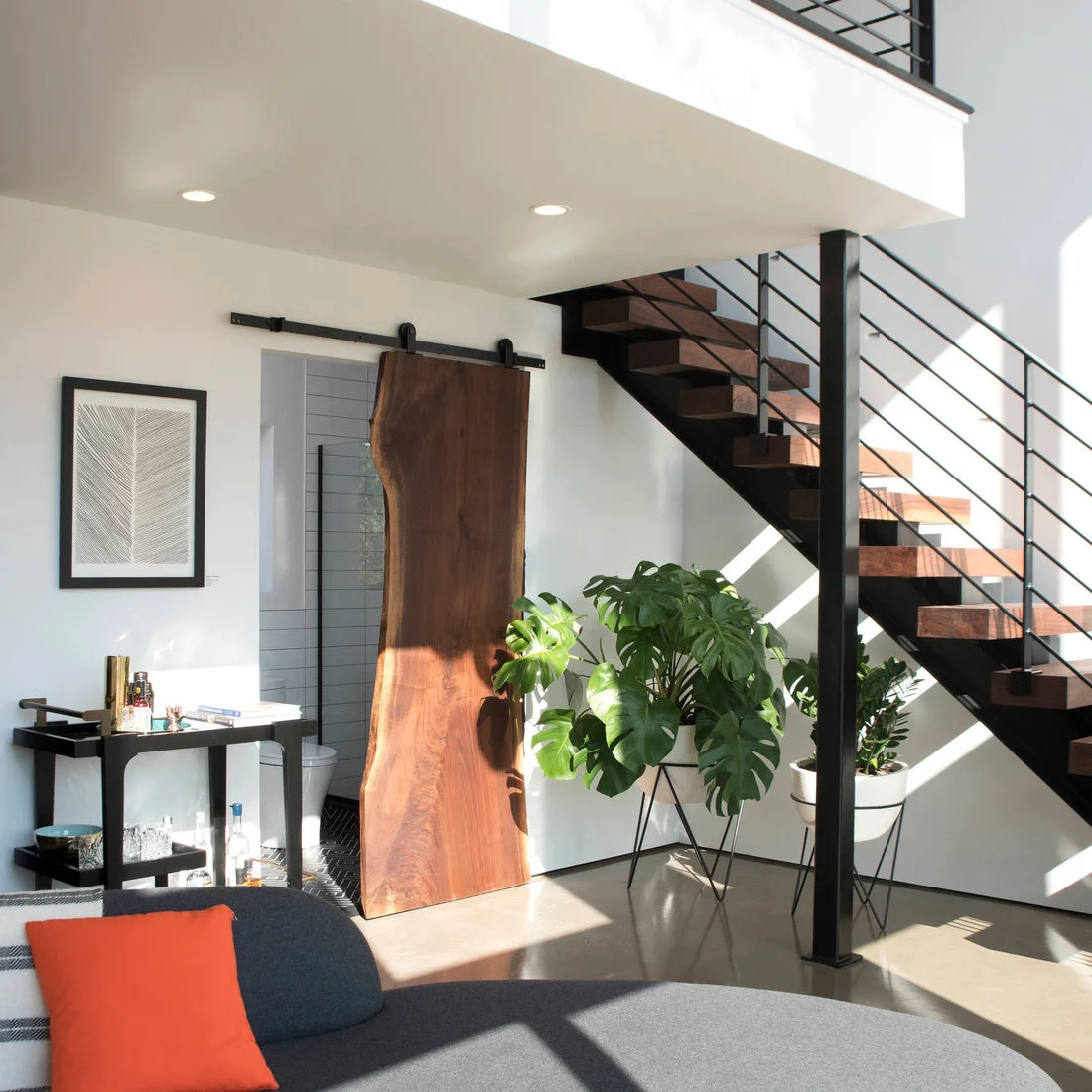 A gray sofa near a black metal stair, timber sliding door, drinks trolley and plants