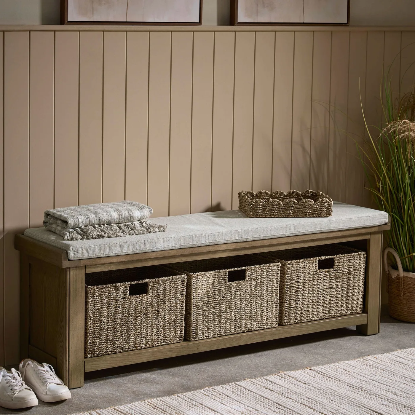A timber bench with pale cushion and three woven baskets below against beige paneling