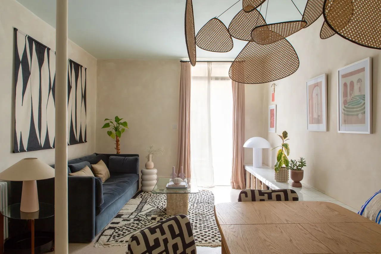 Sculptural woven pendants hang above pale surfaces beside dark seating and graphic art.