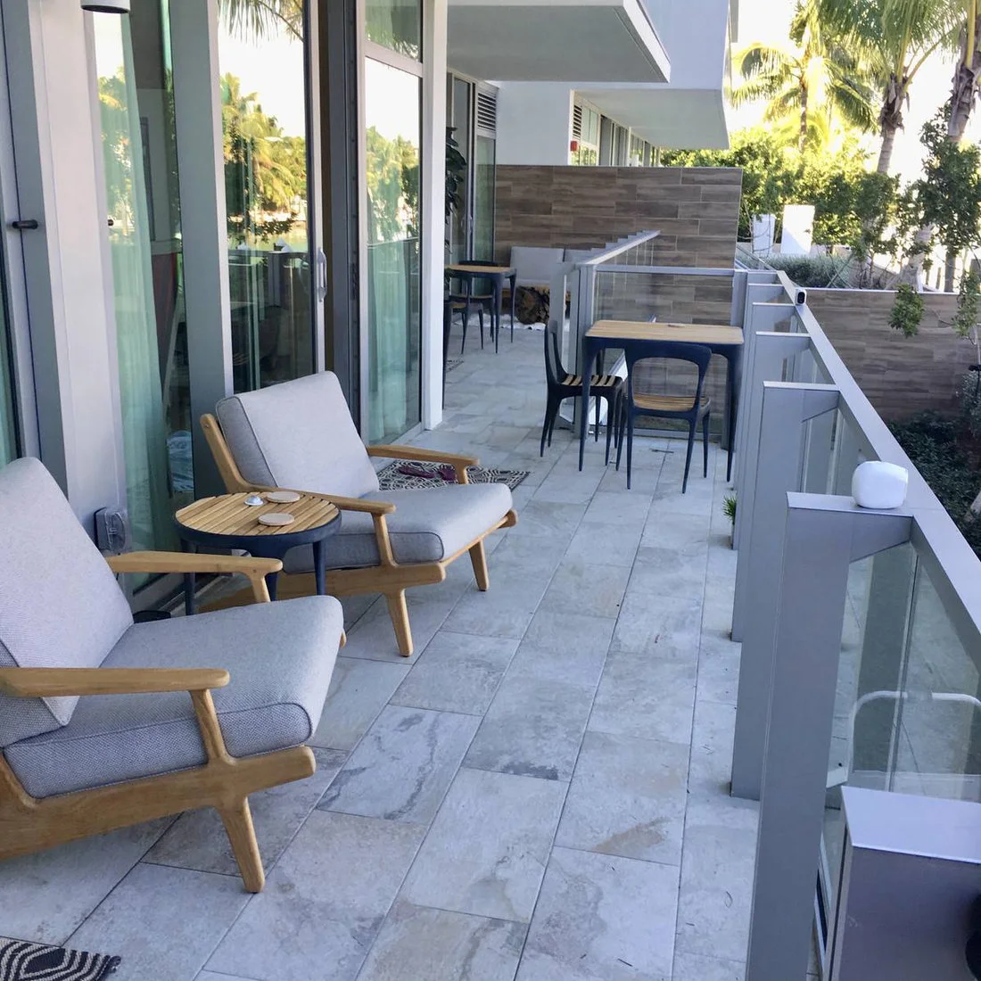 Two lounge chairs and a side table occupy one part of a narrow balcony with dining furniture farther along