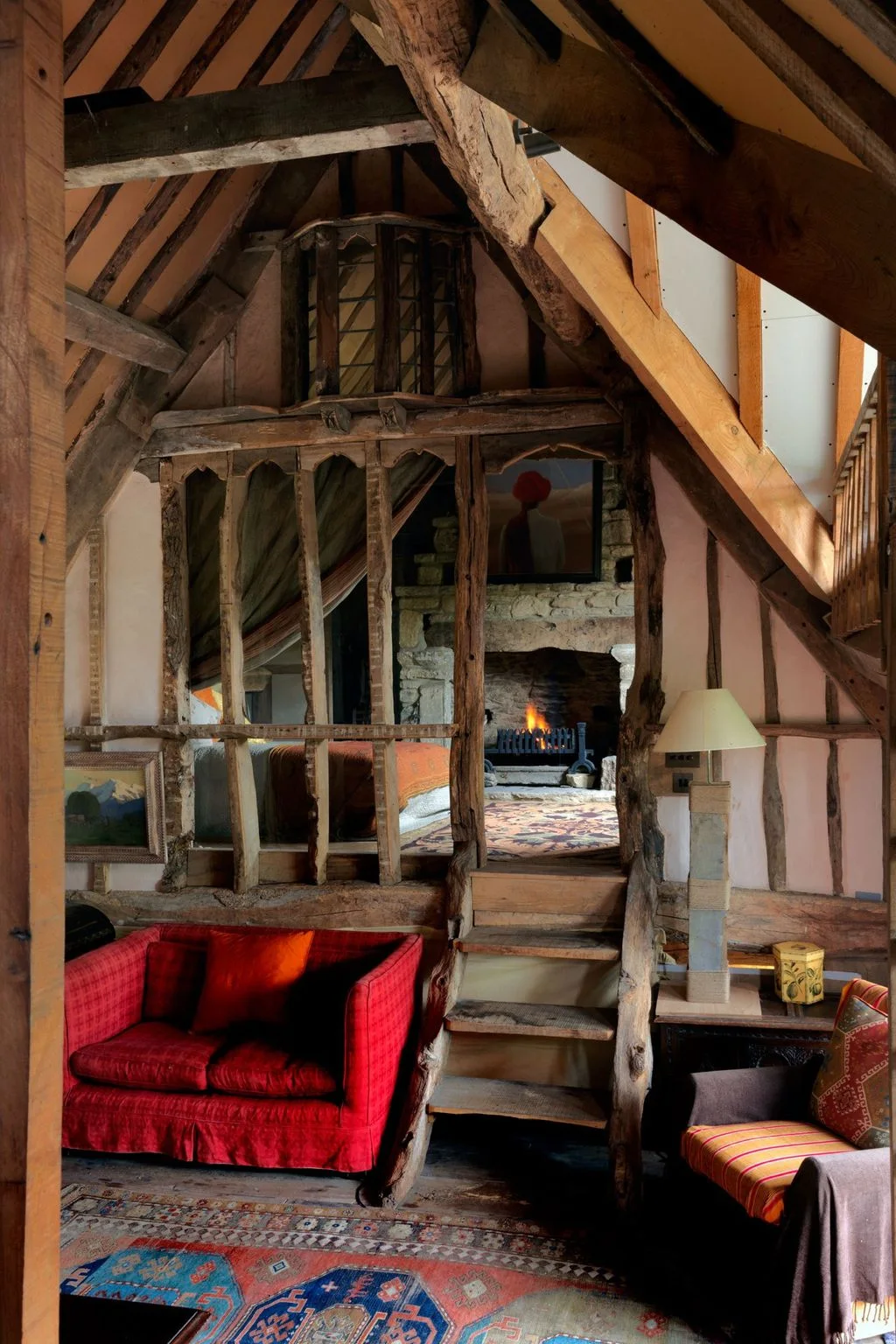 Timber-framed interior with a bright red two-seat loveseat, patterned rugs and steps leading to an upper sleeping area