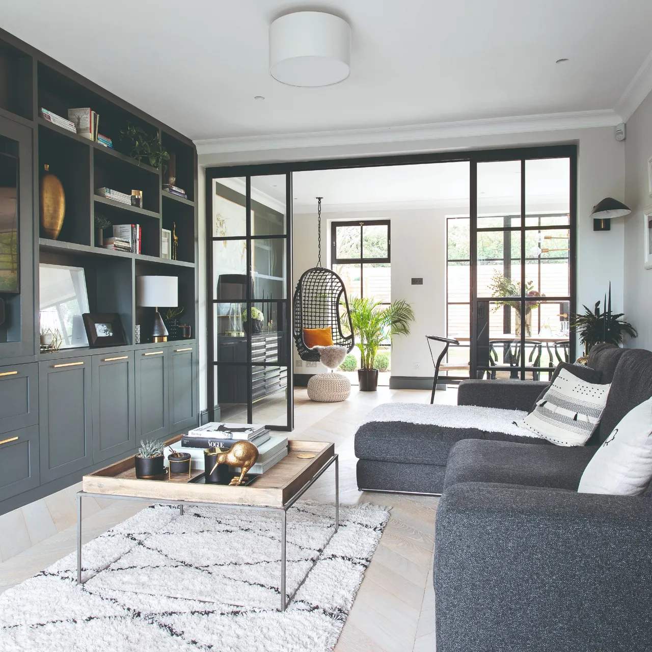 A dark sectional faces a long built-in storage wall with shelves and cupboards