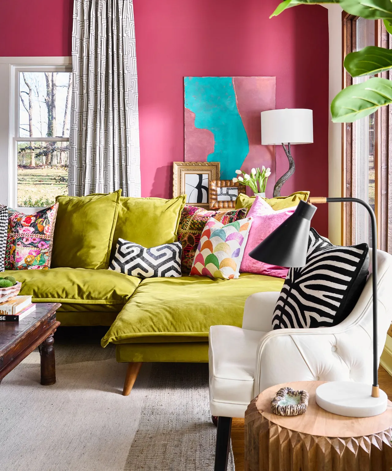 A yellow-green sofa with mixed patterned cushions sits against pink walls beside a pale armchair