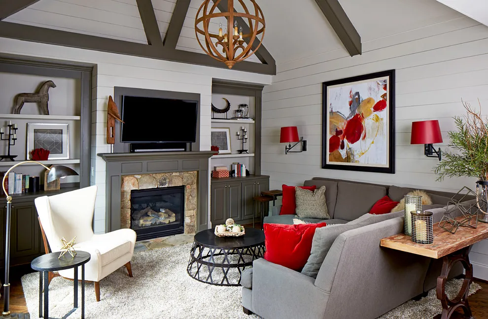 A gray sectional sits beside red cushions, colorful artwork, and a stone fireplace