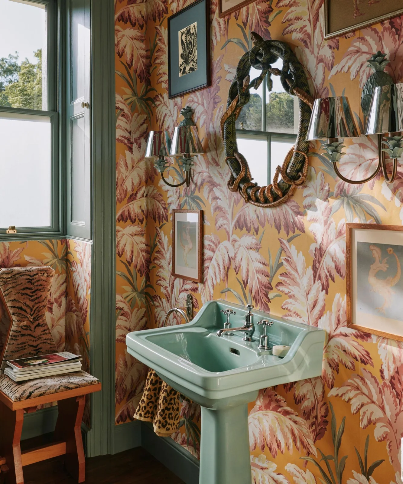 A green pedestal basin and green window trim stand against botanical wallpaper with pink foliage on a warm background.