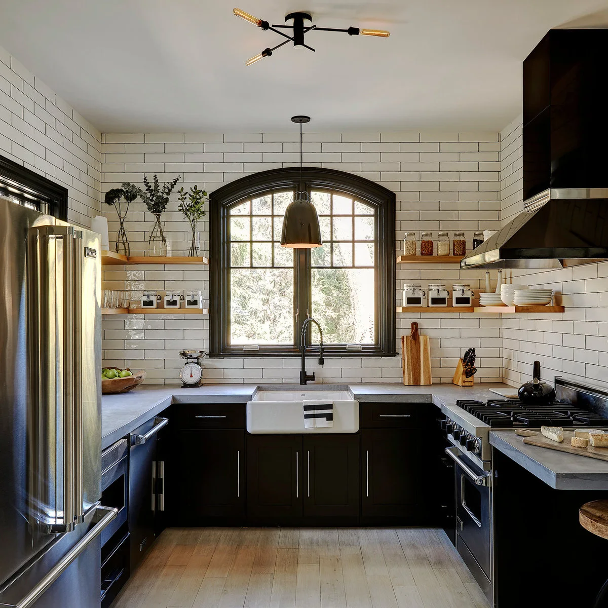 A single pendant hangs before an arched dark-framed window above a white sink, with wood shelves on both sides.