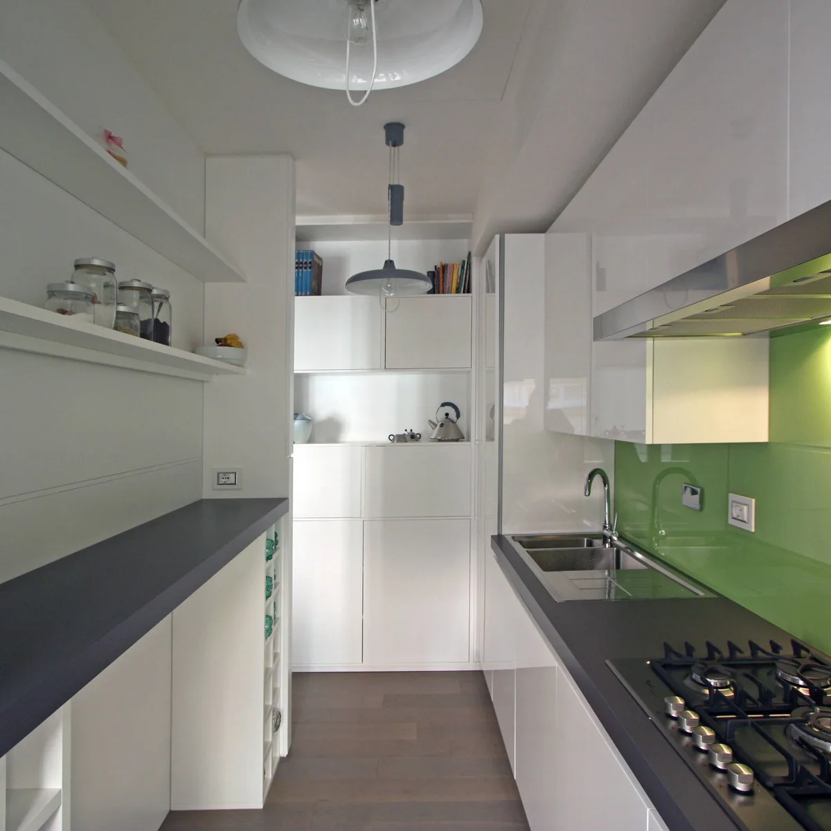 Narrow white galley kitchen with open shelves on one side and green backsplash at the sink