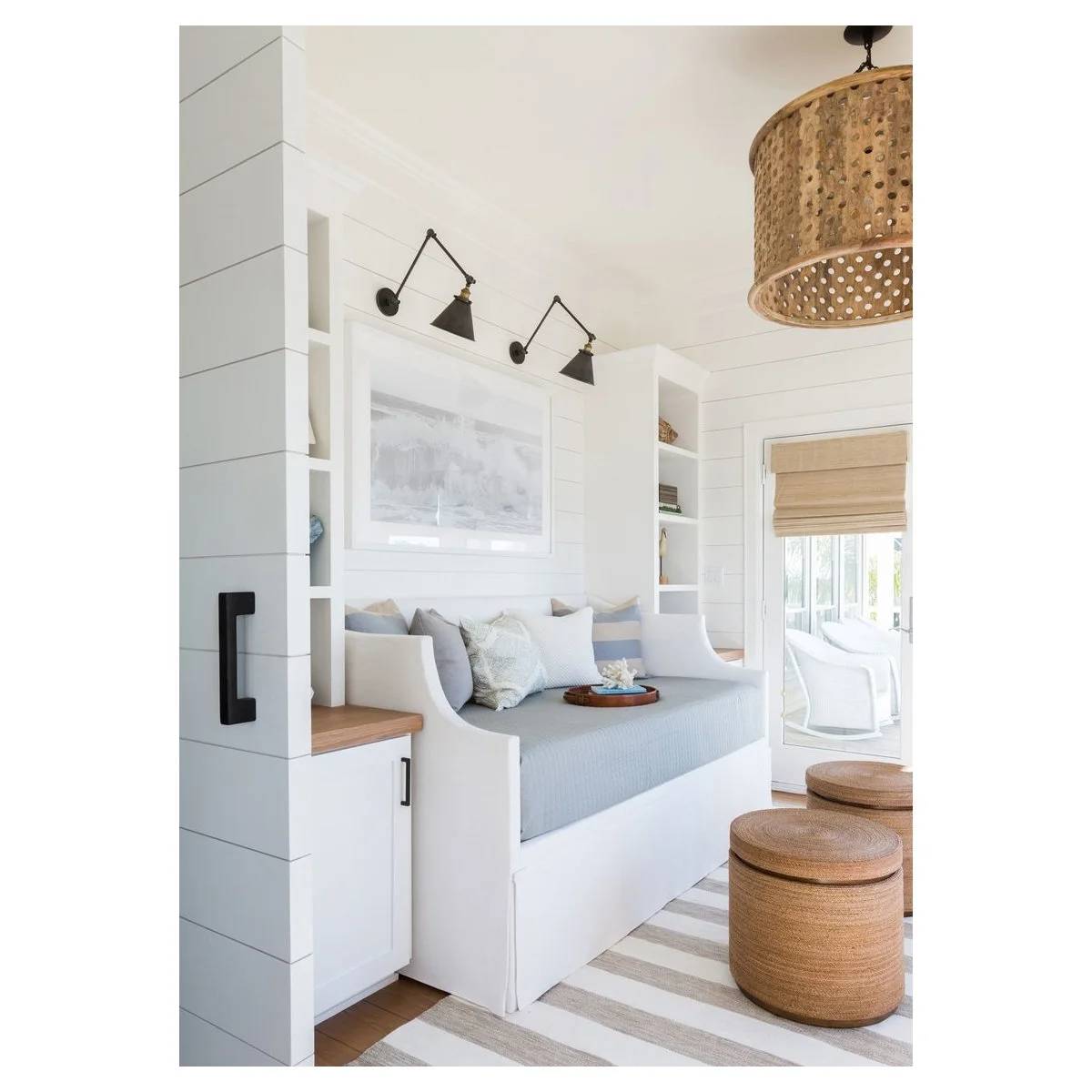 A pale blue-covered white daybed sits between slim shelves and cabinets beneath two adjustable wall lamps.