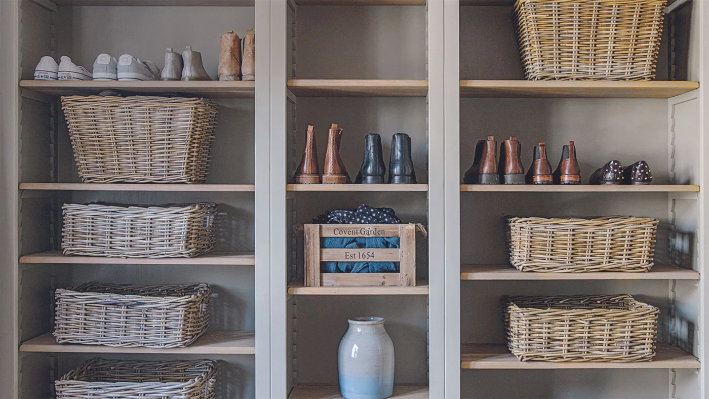 Gray open cabinets have adjustable wood shelves holding shoes, boots, baskets and a wooden crate.