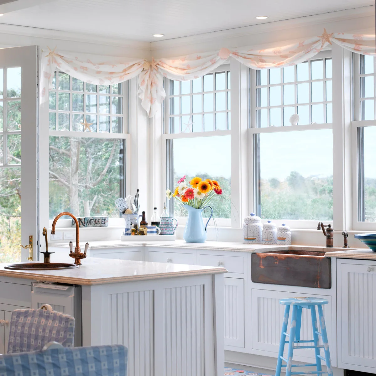 Pink coral-pattern valances above corner windows in a white kitchen