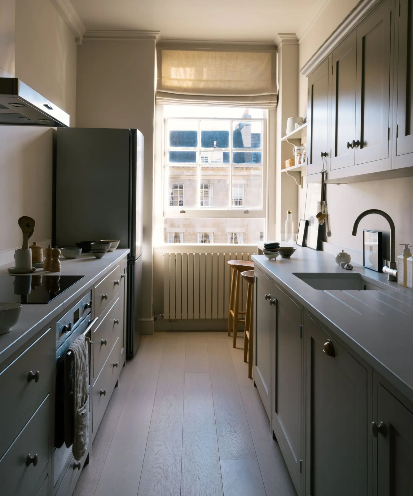 Narrow gray galley kitchen with a window at the end and two stools beside a shorter counter