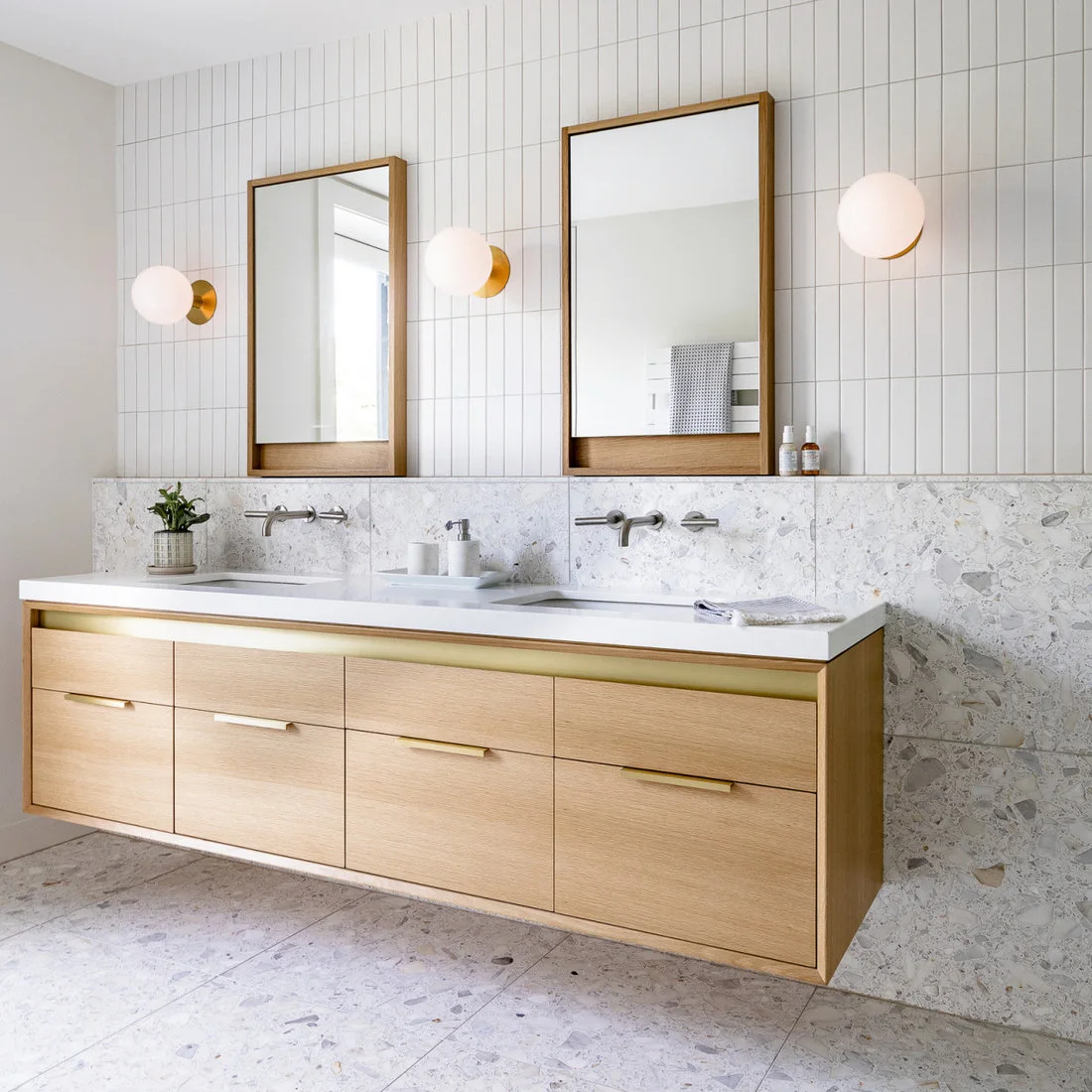 A pale terrazzo backsplash and floor frame a floating double vanity beneath white vertical tiles.