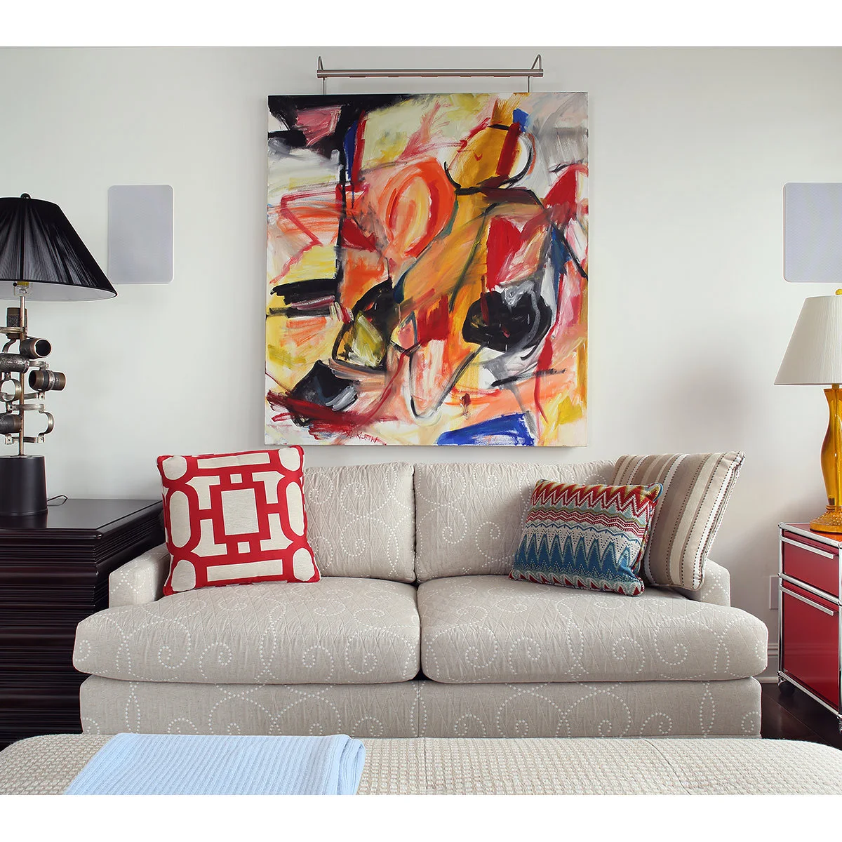 Cream patterned sleeper sofa between drawer units beneath a colorful abstract painting