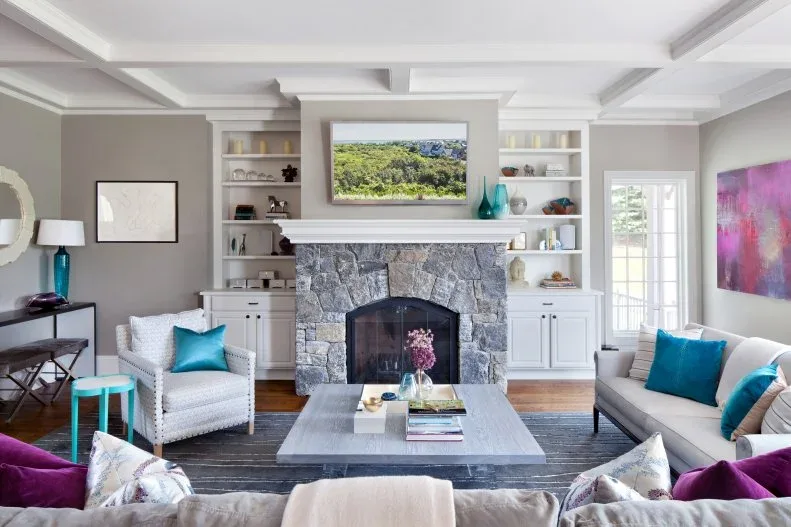 Gray stone-faced fireplace under landscape picture with white shelves, cabinets and turquoise room accents