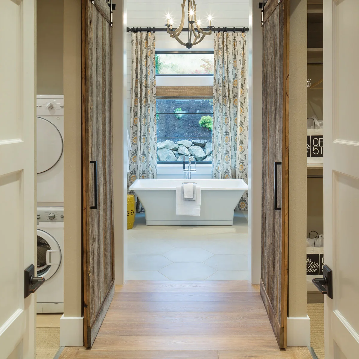 Patterned full-length curtains and a woven-looking shade frame a tall window behind a rectangular white bath.