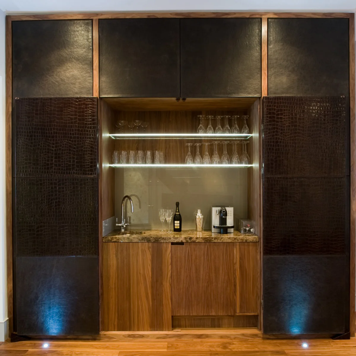 Basement drinks niche with open folding doors, lit glass shelves and a small sink