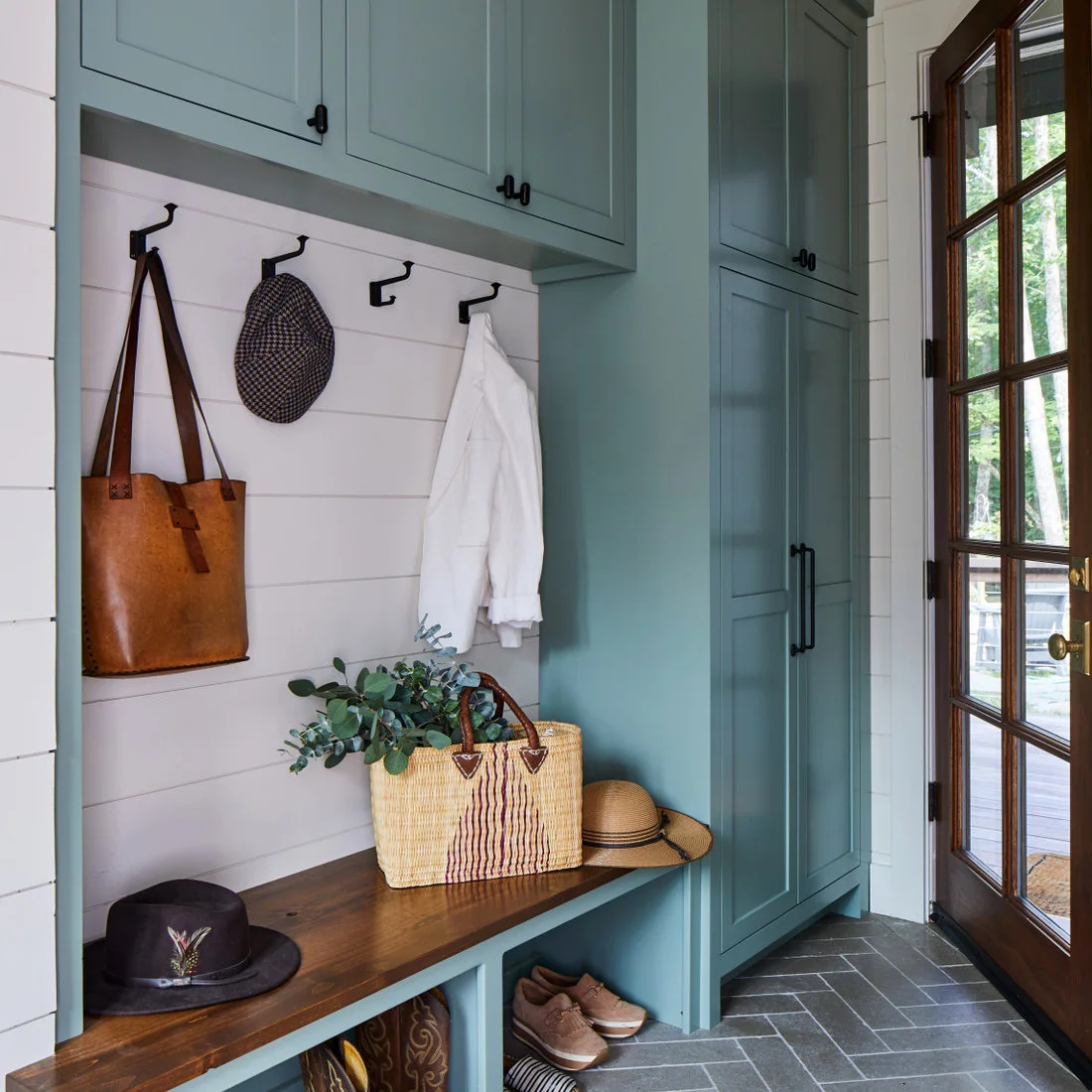 Blue green entry cupboards and a timber bench beside white boards and a dark herringbone floor