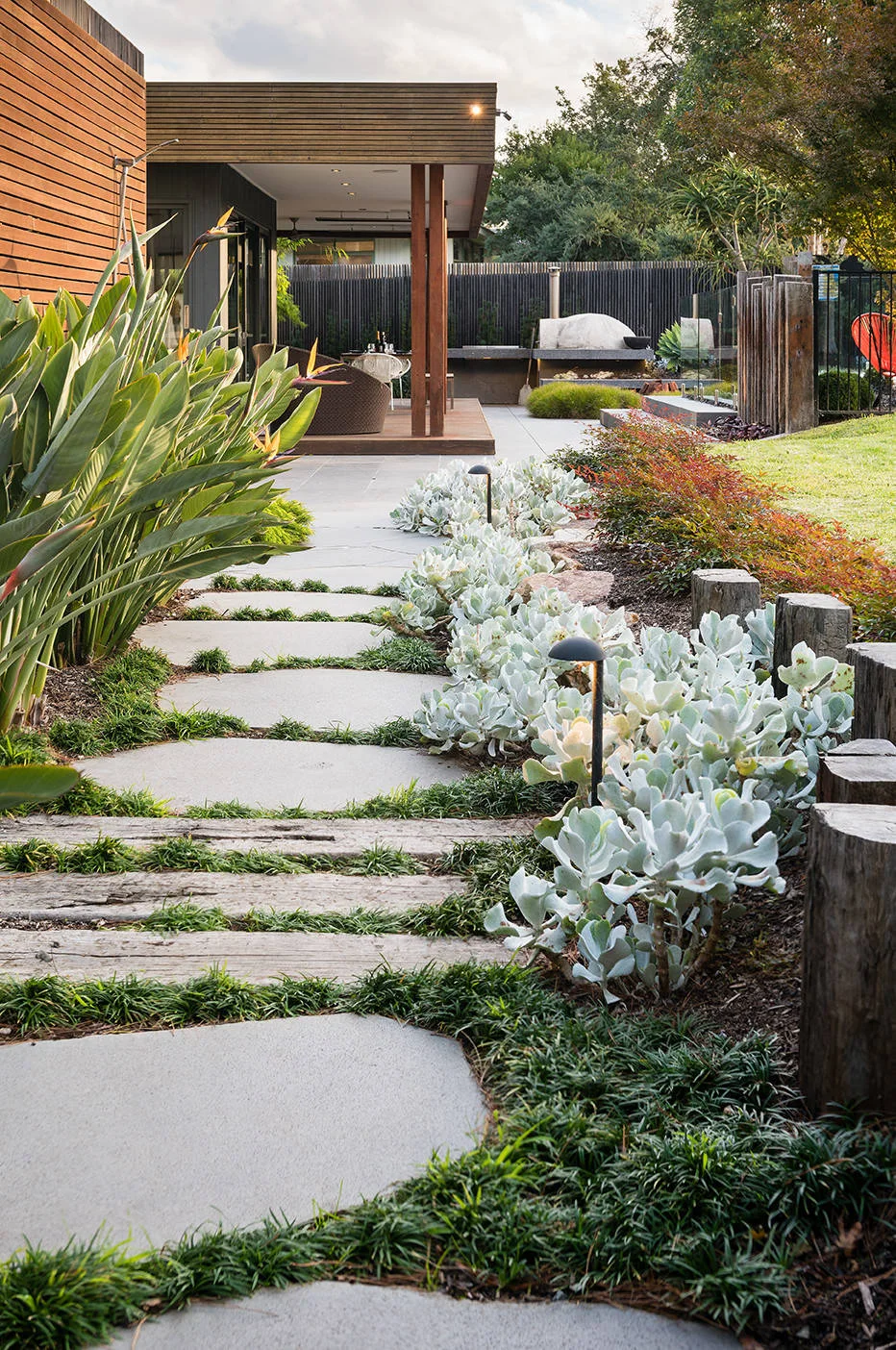 Pale garden stepping stones pass silver foliage and low path lights toward a covered patio