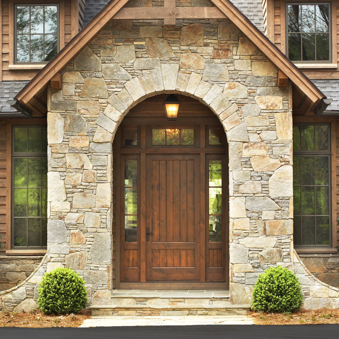 A timber front door and sidelights beneath an arched stone entrance and pitched porch roof