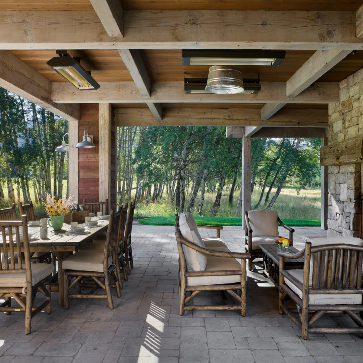 A solid timber roof spans a dining table on the left and a lounge group on the right, with open views to trees.