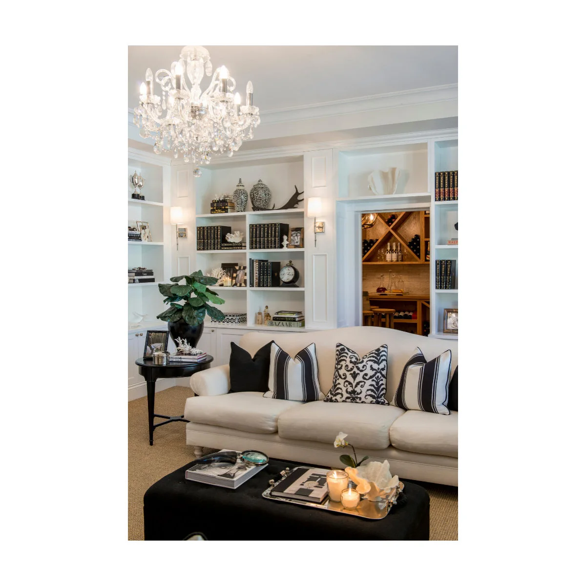Pale sofa with black-and-white cushions, dark ottoman and white shelves behind