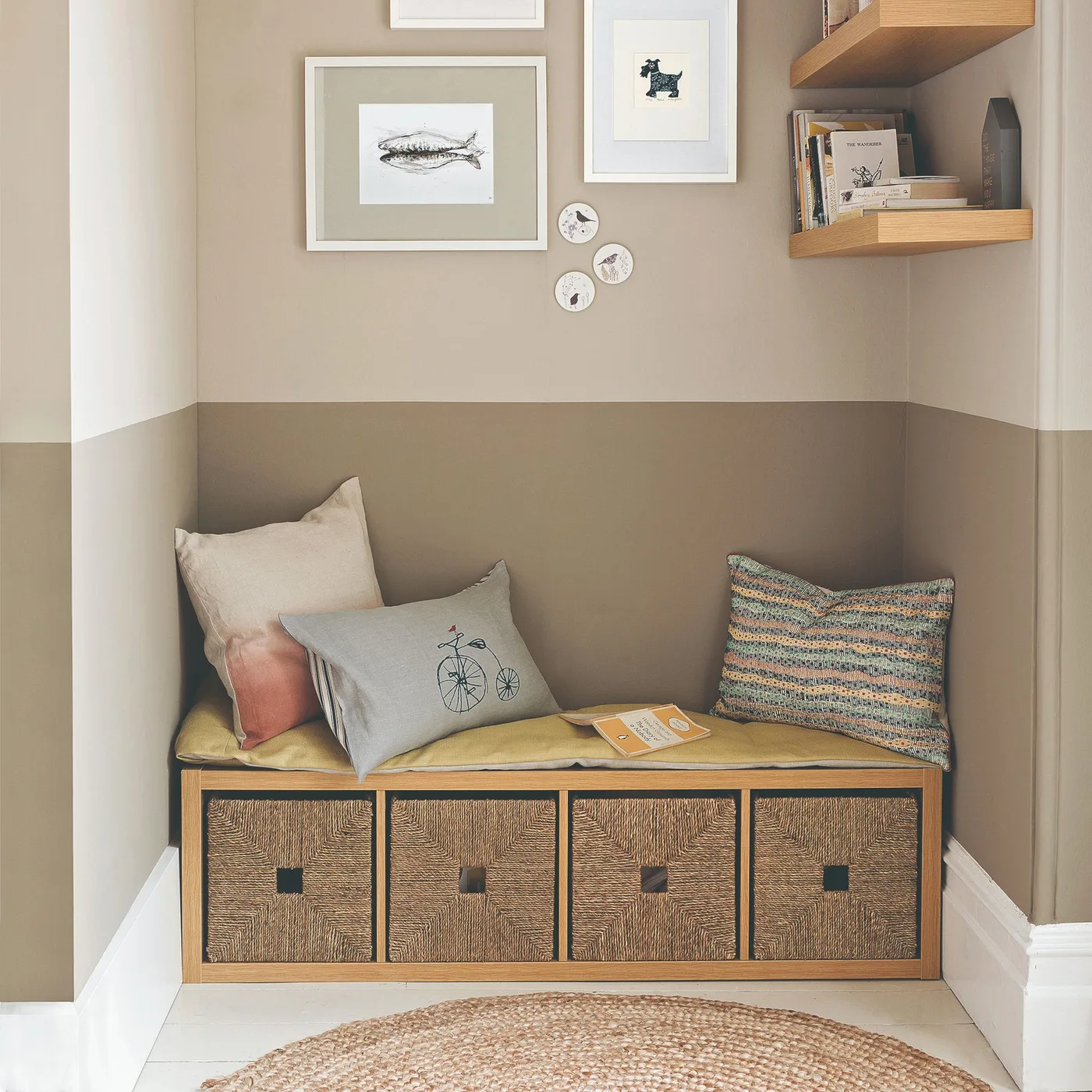 Woven-front drawer unit beneath two-tone neutral wall, framed pictures, open shelves and cushions, with round woven rug.