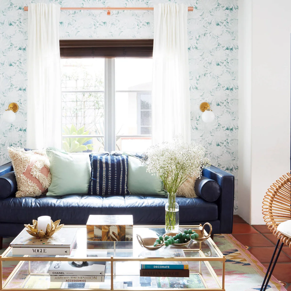 Pale floral wallpaper surrounds a window above a dark blue sofa with mint and patterned pillows.