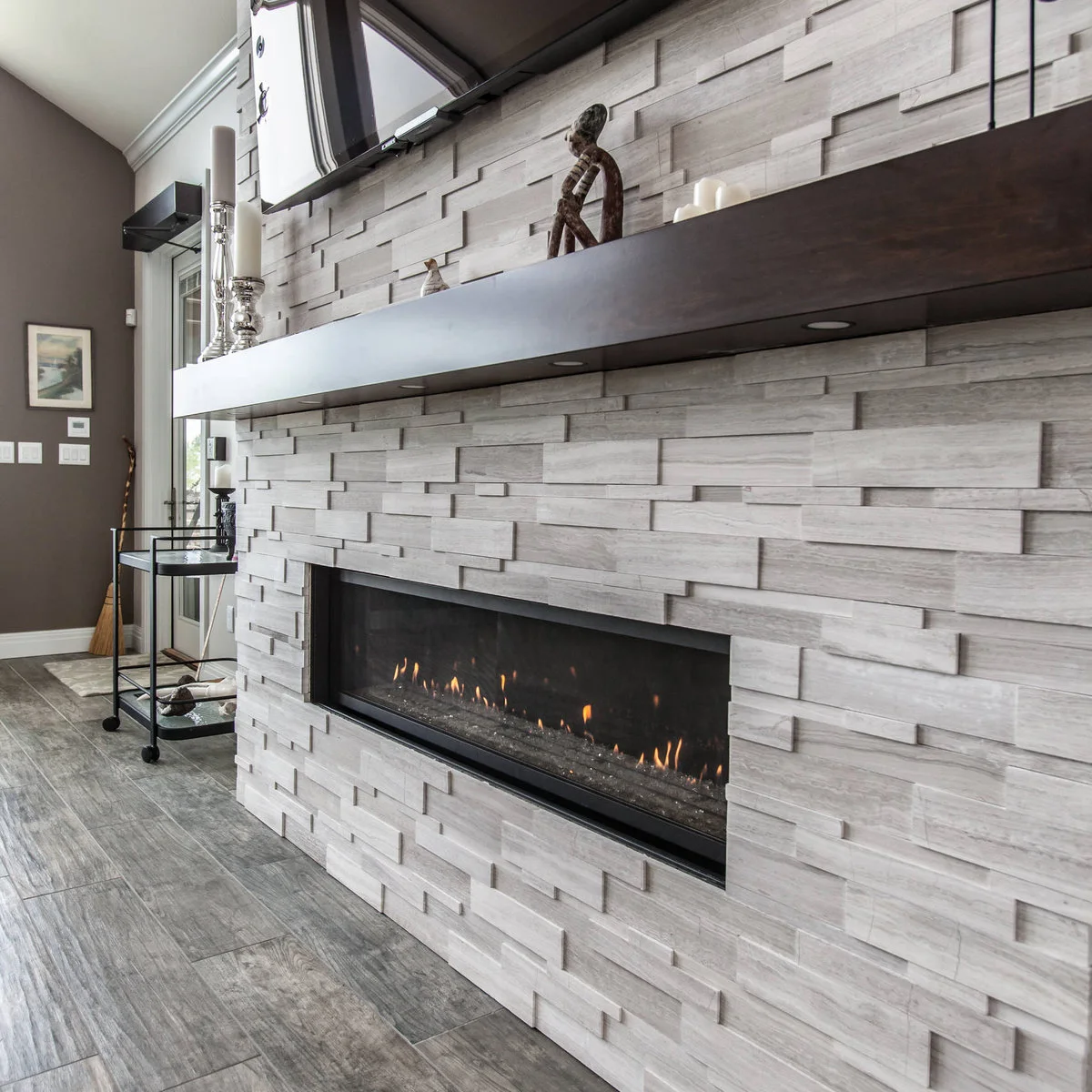 A close view of a pale layered fireplace wall with a long dark mantel, small under-shelf lights and the lower edge of a television.