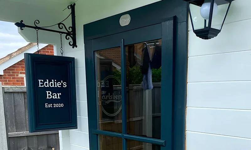 Dark glazed garden pub door beside a hanging sign and black lantern on pale boards