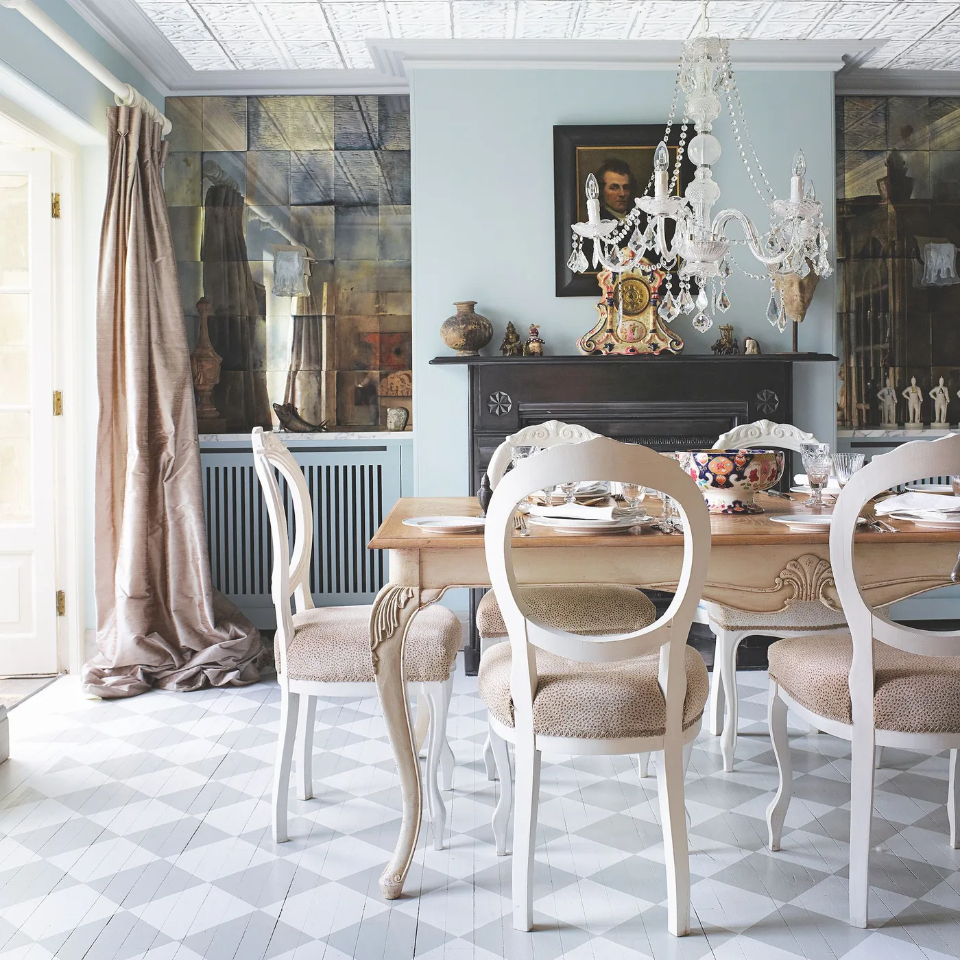 Mottled mirror panels beside a black fireplace behind a dining table with pale ornate chairs