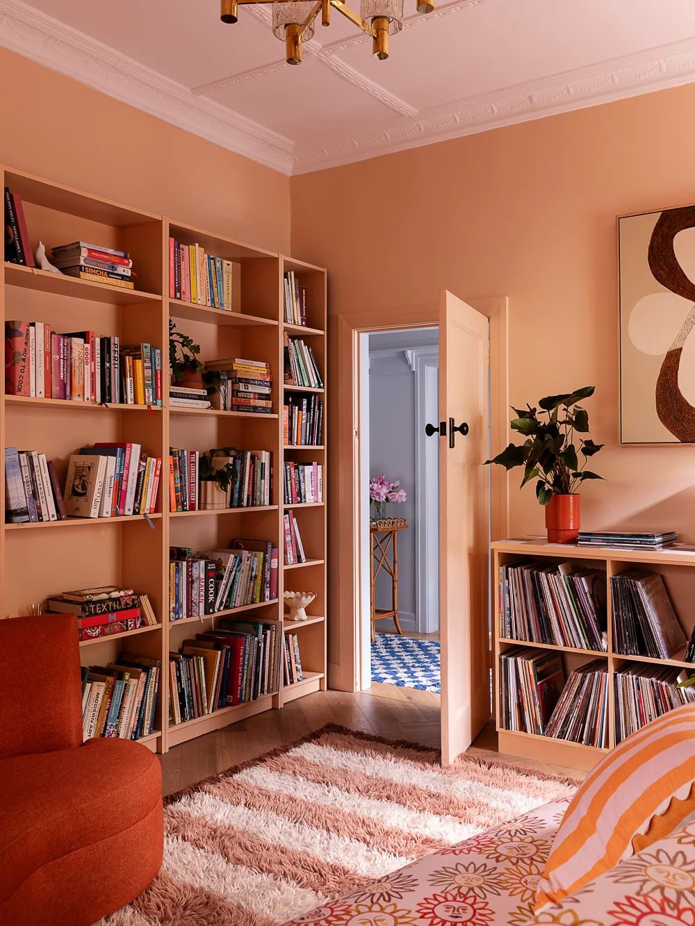 Peach-colored shelves filled with books line a warm peach room beside a doorway, lower cubbies and patterned seating