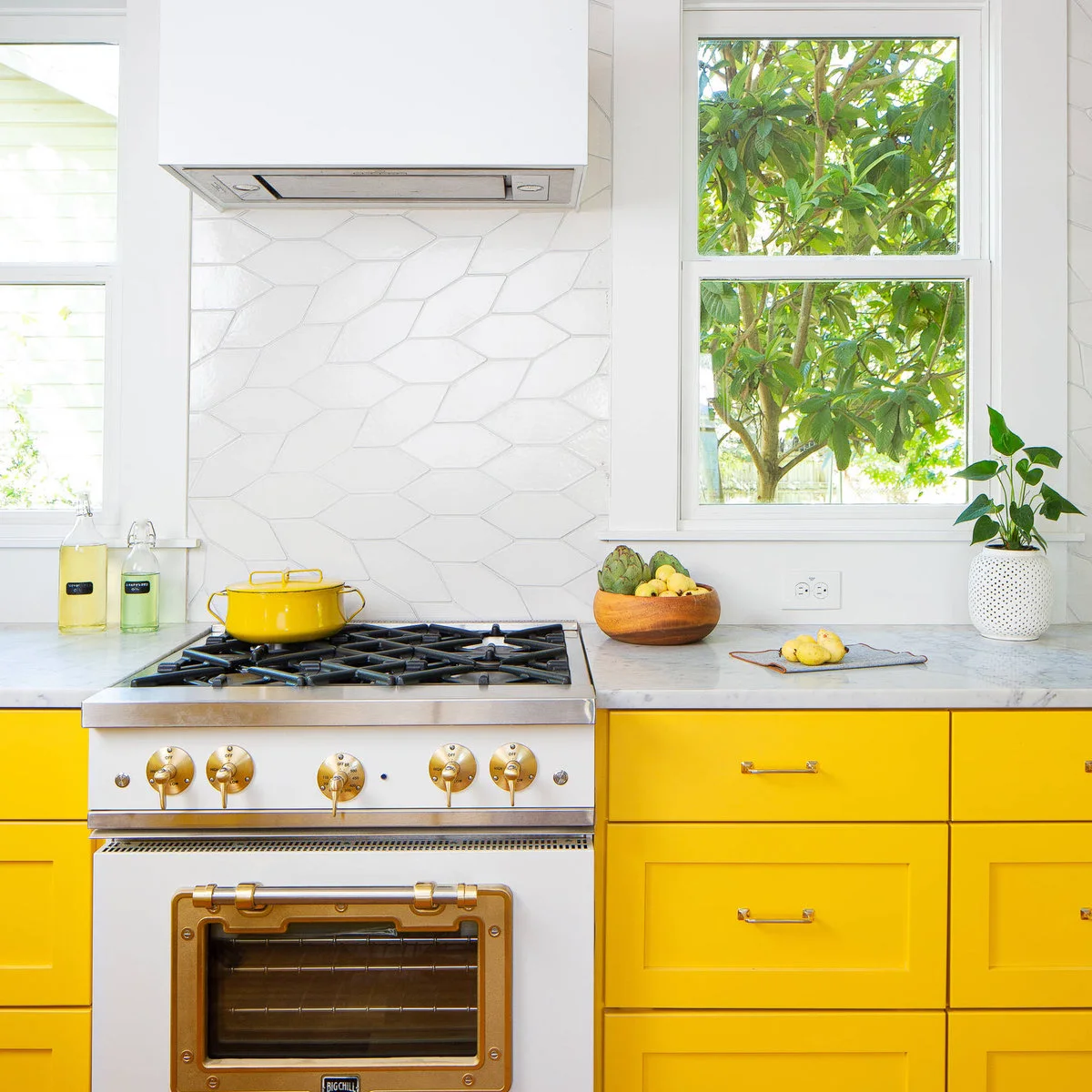 Yellow kitchen drawers beside a white range with brass-colored details and a white tile backsplash