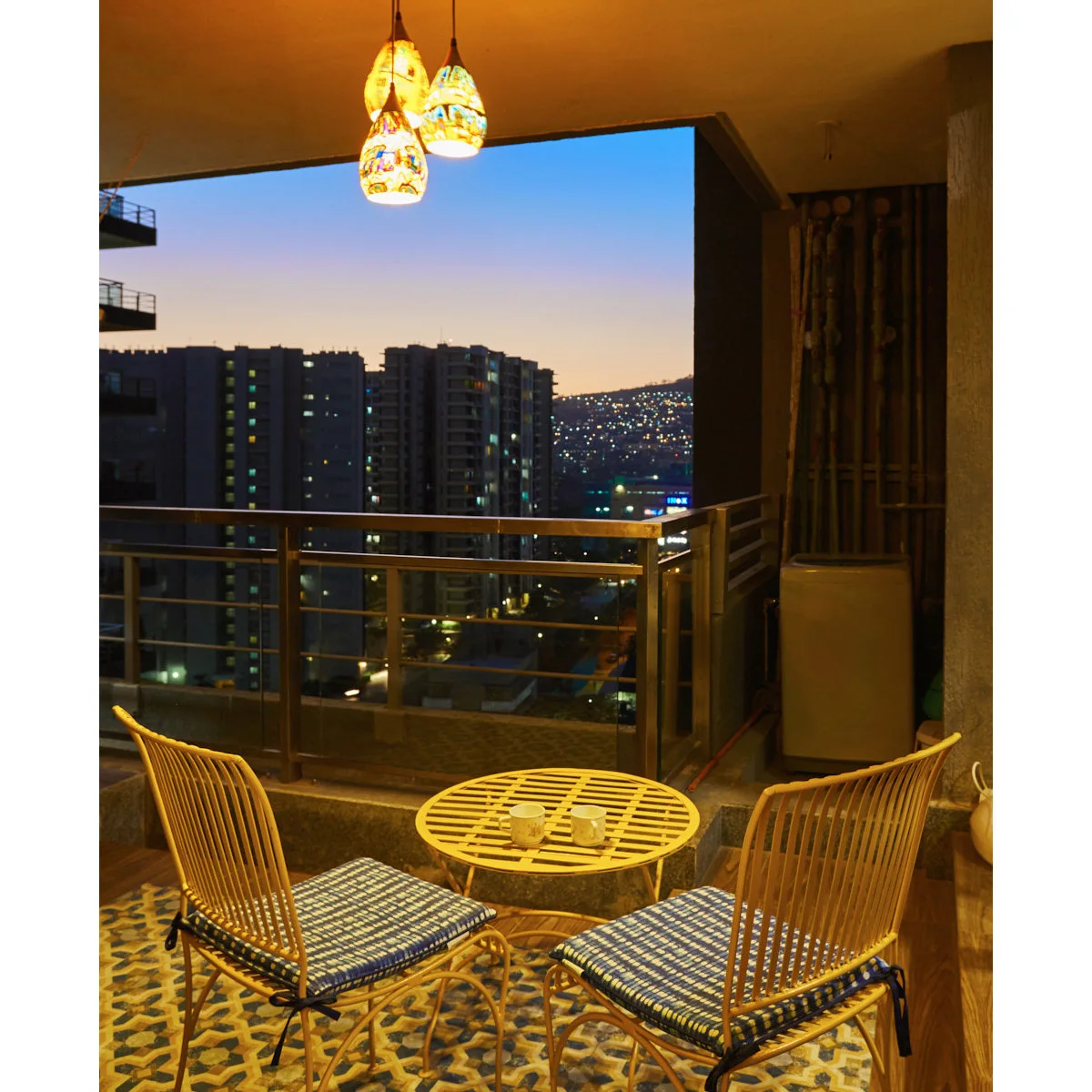 Sheltered apartment balcony with two wood-colored chairs, round table and hanging lights