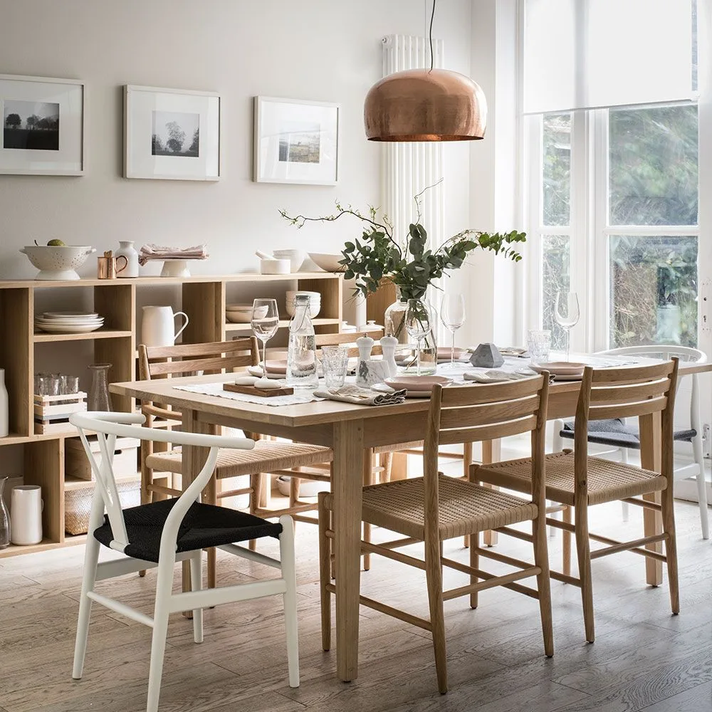 Copper-toned dome pendant above a wood dining table beside a window and open dish storage
