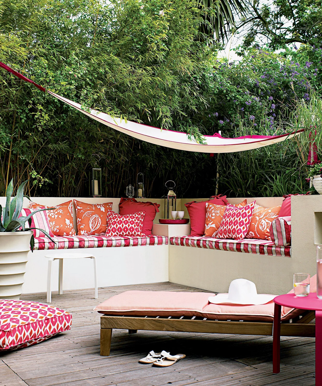 Dense tall foliage and a pale canopy shelter built-in outdoor seating with red cushions