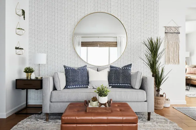 A round mirror hangs above a pale sofa with dark blue pillows.