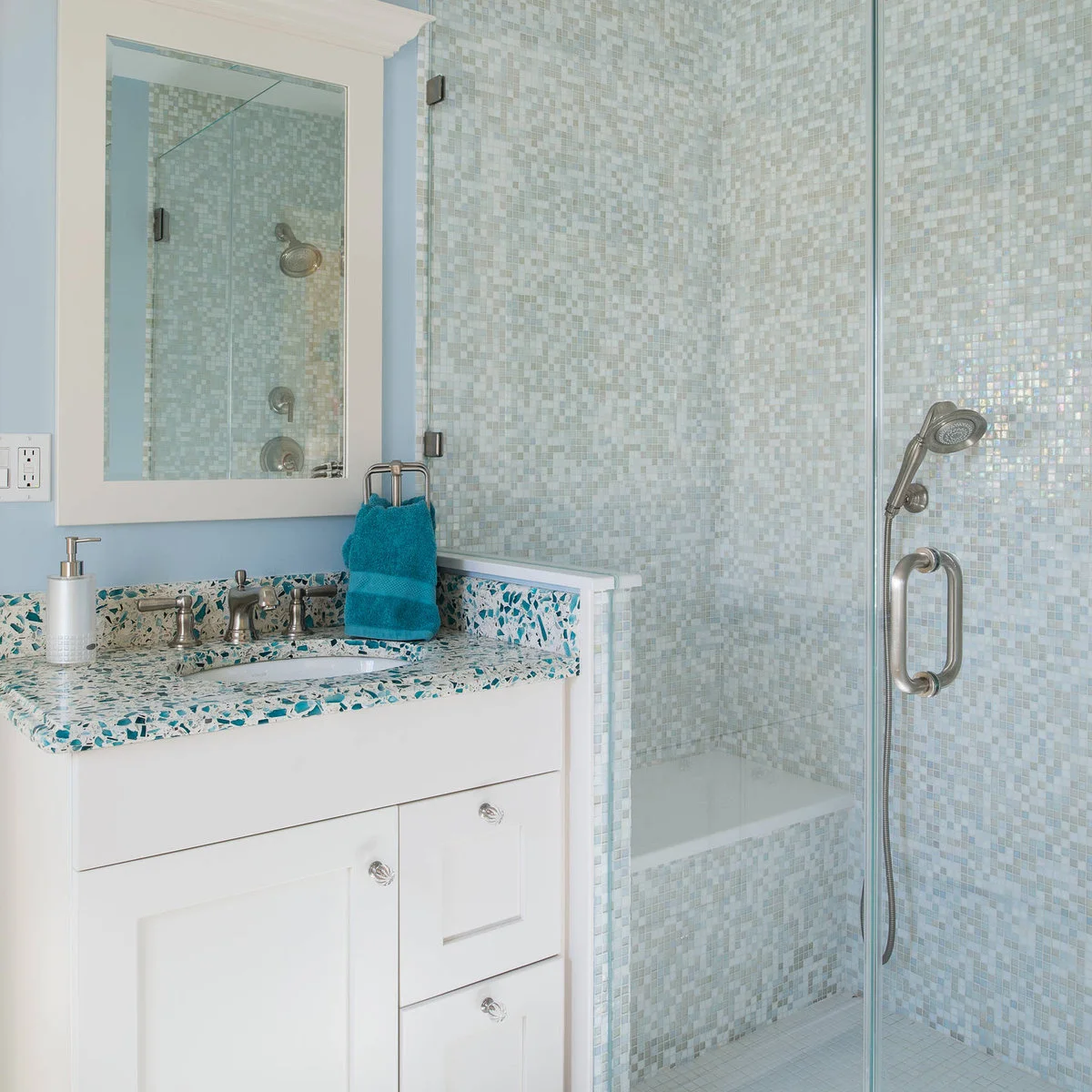 Pale blue mosaic shower with a built-in bench beside a turquoise-speckled counter