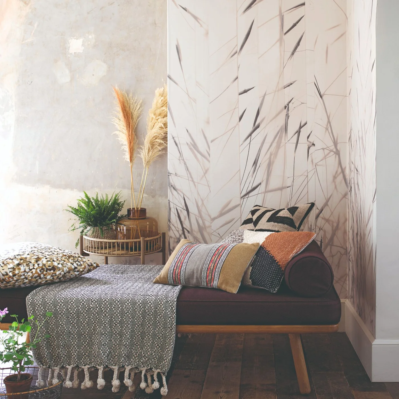 A dark upholstered daybed with timber legs sits beside botanical wallpaper and a small plant table.
