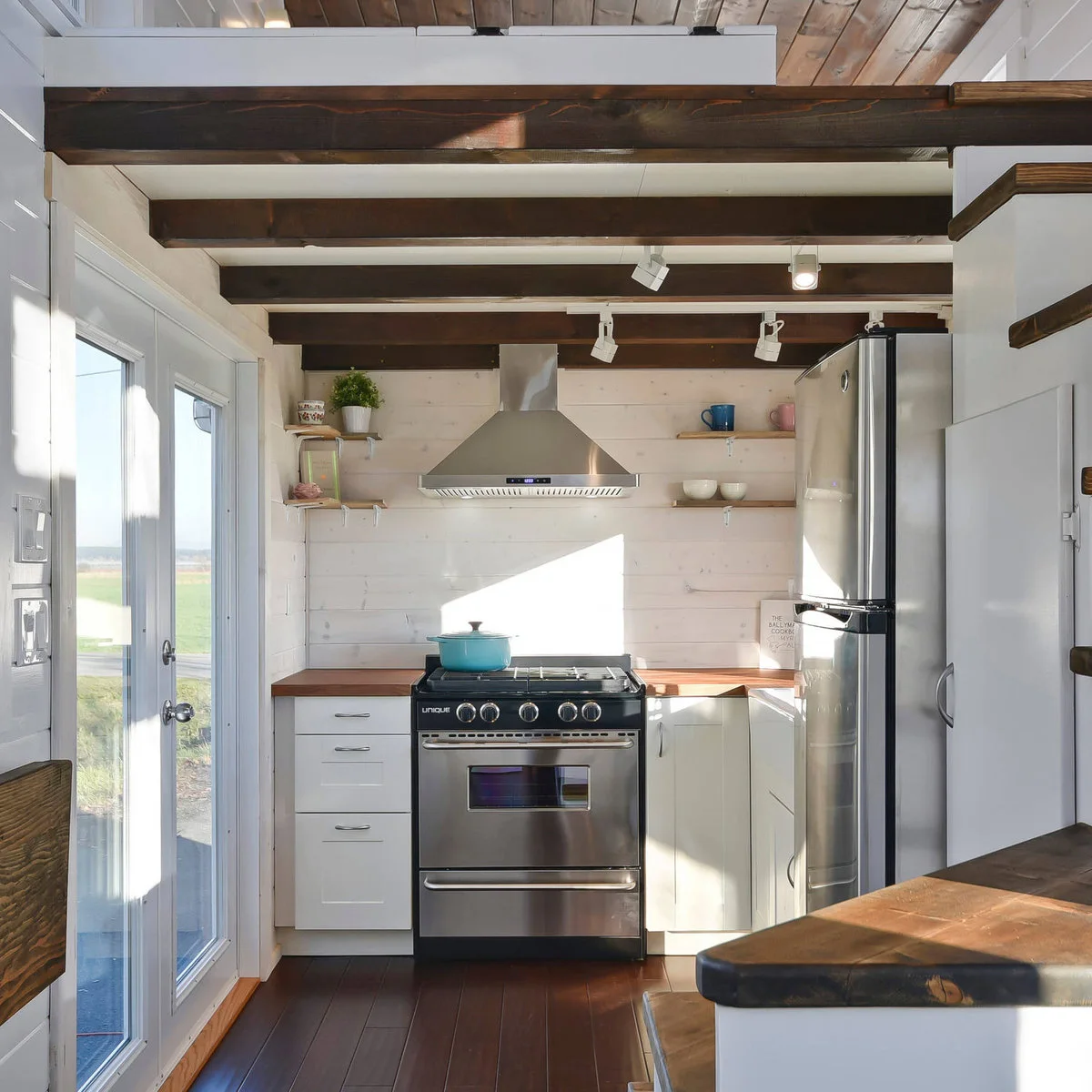Small white kitchen beneath exposed beams with a glazed door beside the range