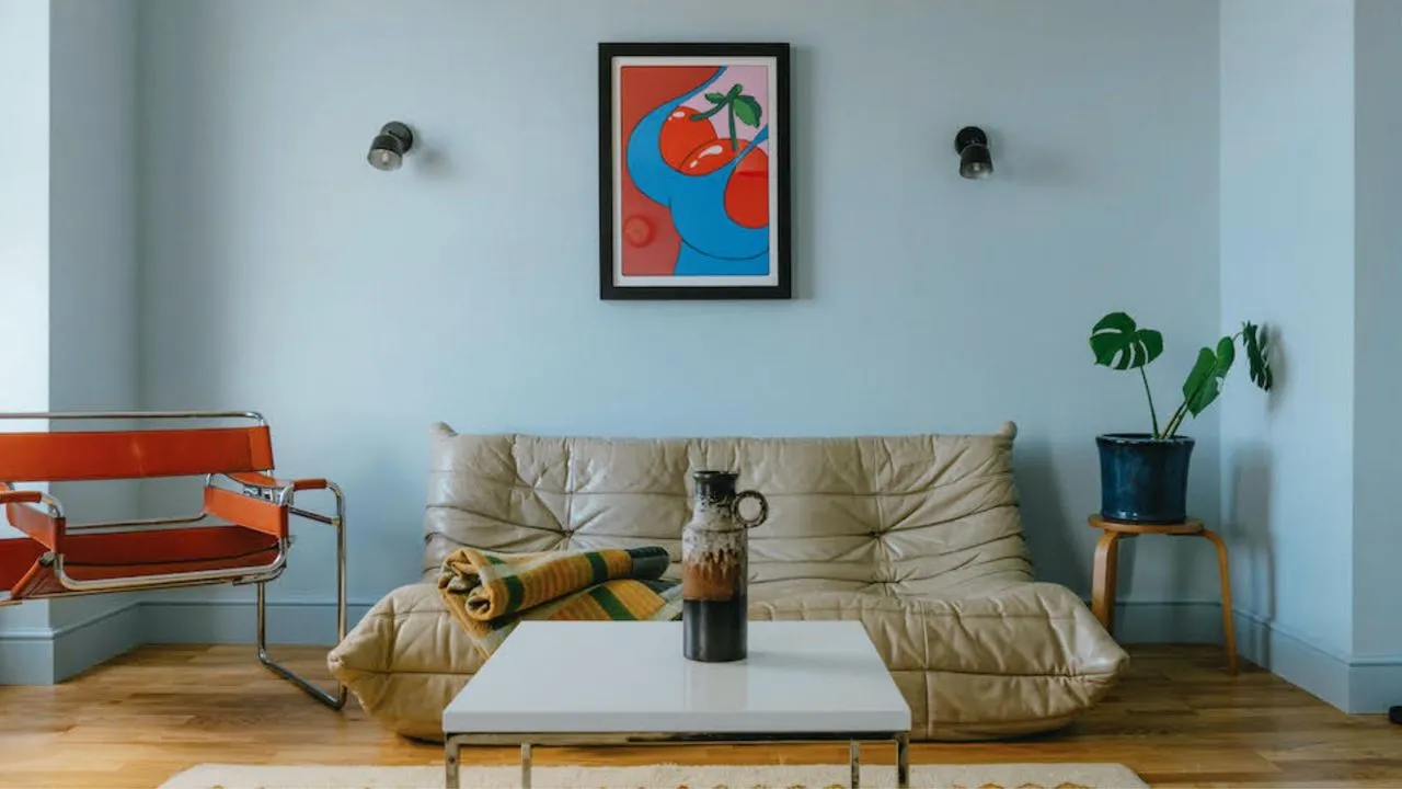 A pale blue wall stands behind light seating and a bright framed artwork.