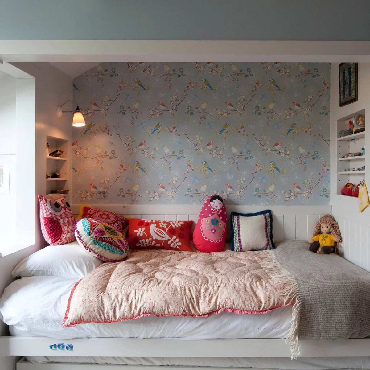 Daybed in a pale alcove with bird-patterned wall covering and colorful cushions