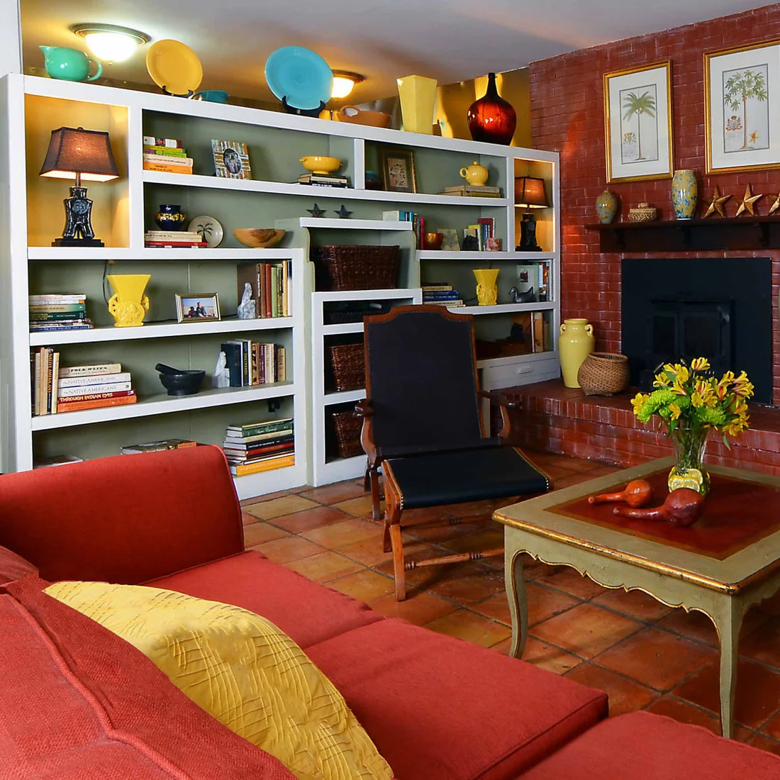 Orange floor tiles sit below a red sofa, timber chair, colorful shelving and a brick fireplace.
